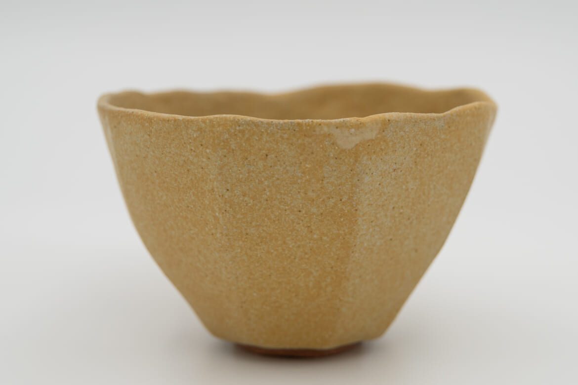 Front view of Unfolding, a warm ochre stoneware tea bowl with a gently undulating rim, by Celeste Ortelee.