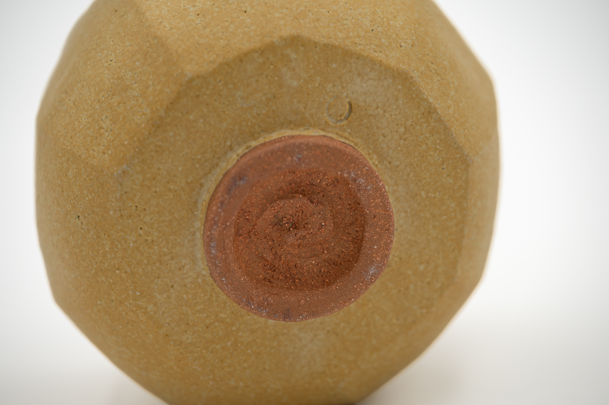 Detail of the underside of Holding, showing the reddish unglazed foot, maker's mark and textured ochre-glazed surface.